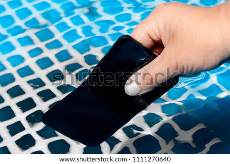 a mobile phone of a dark color lies on the bottom of the pool. The water is a little muddy.