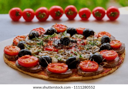 Veggie pizza with mushrooms, black olives and herbs on the gray kitchen table decorated with fresh cherry tomatoes. Pizza background. Close up view