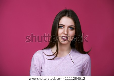 Portrait of beautiful dissatisfied brunettes girl on dark pink background.