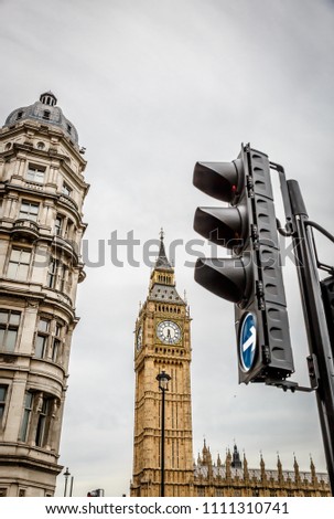 Vertical view of a traffic light with the Big Ben Clock Tower and a old building in the background. London, UK