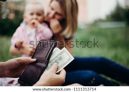 Earning money for family. Male hand with wallet and US dollar bills at family blurred background. Financial support, business, family, alimony, maintenance, investing in children concept Royalty-Free Stock Photo #1111313714