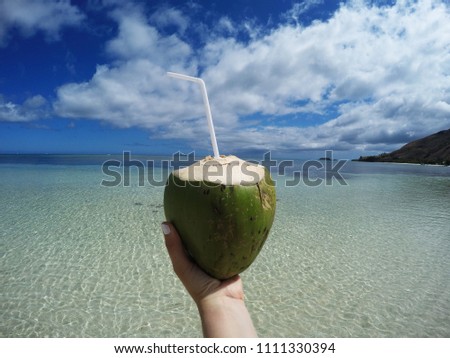 Coconut cocktail decorated with straw and Fiji flowers. White sand beach, palm trees, ocean on the background. Photo taken in Fiji Islands-Yasawa group, Pacific Ocean.