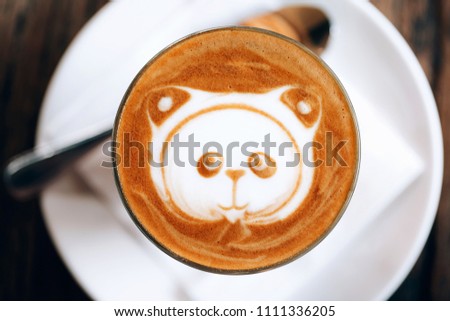 Panda latte art in cappuccino cup on wooden table. Pattern on coffee foam.