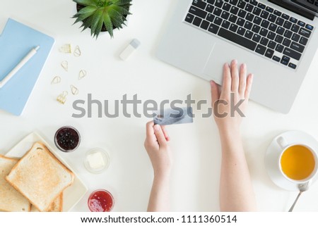 Top view of woman hands holding credit card, business lunch concept, online shopping, workspace with laptop, mobile phone, flowers and notebook, toast, flat lay.