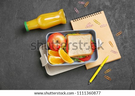 Flat lay composition with lunch box, appetizing food and stationery on dark background