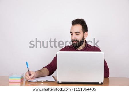 Handsome businessman wearing a formal outfit, sitting in his office work on his laptop and writing notes