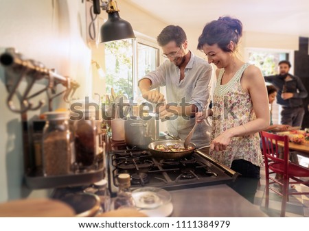 Mixed group of friends having fun while cooking a meal in a warm and welcoming kitchen. a couple takes care of the pots on the stove , while the sun comes in through the window Royalty-Free Stock Photo #1111384979