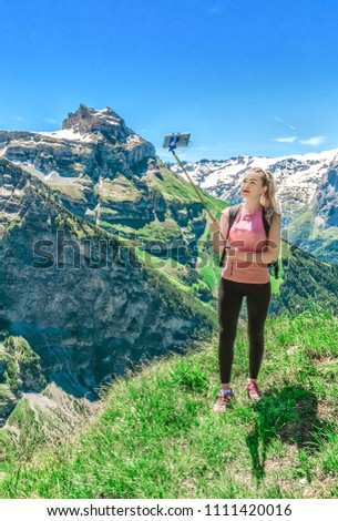 Girl traveler photographing herself, making a salfi on the smartphone, against the backdrop of the mountain peaks of Switzerland
