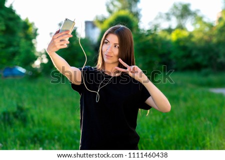 Happy Asian girl smiling at the camera. To call by video call. Speaks on the phone listening to music. Hand gestures. Hello. Summer in the field on a green meadow. He speaks in social networks.