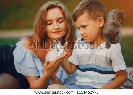 beautiful red-haired mother with her son playing in the summer park and with kitty and rabbit;