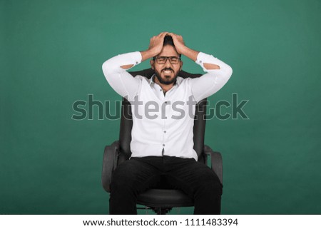 Young tired man sitting on office chair touching his head with closed eyes on a green background.