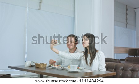 Happy young couple taking selfies with food on smartphone at a restaurant