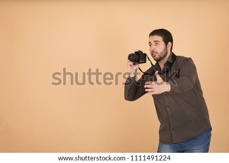 Handsome photographer wearing a casual outfit, holding his camera taking photos and he is adjusting the pose of the model, standing on an orange background