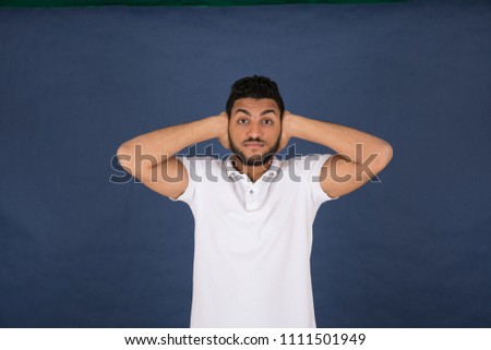 Young man standing puts his hands on the ears on a blue background.