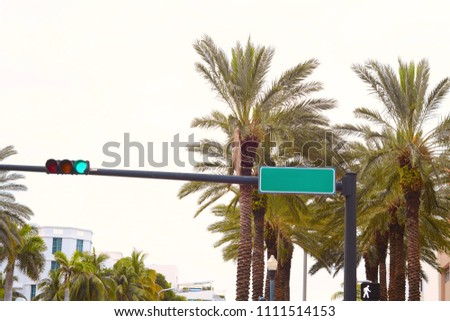 Blank green traffic road sign against the palm trees and sky