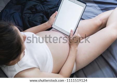 Close-up Of  Pregnant Woman Sitting On bed Using Digital Tablet,