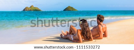 Hawaii travel summer vacation couple on hawaiian tropical beach in Lanikai, Oahu, Hawaii, US. American tourists people on holidays lying down, panoramic banner crop with moke islands in background. Royalty-Free Stock Photo #1111533272
