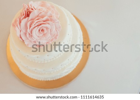 Three-tiered white wedding cake decorated with flowers from mastic on a white wooden table. Picture for a menu or a confectionery catalog. Top view.