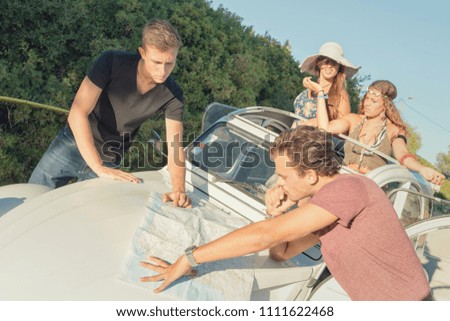 Vintage style image of men looking at a map over a car in countryside with girls waiting.