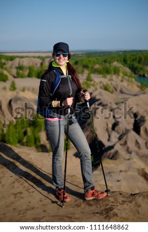 Image of smiling tourist girl with backpack and walking sticks on hill