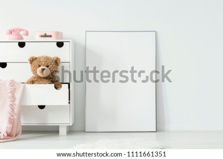 Plush toy and pink blanket in cabinet next to empty white poster in baby's room interior. Real photo. Paste your photo here Royalty-Free Stock Photo #1111661351