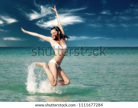 Young woman in white bikini playing in the sea. The girl standing in the water and jumping. Summer vacation concept