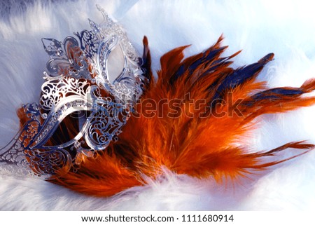 beautiful filigrane ornamental silver venice mask with radiant feathers on white fur structure.