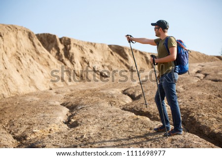 Photo of athlete with backpack and walking sticks pointing with hand to side