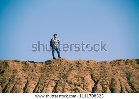 Picture of afar of tourist man with sticks for walking on hill against blue sky