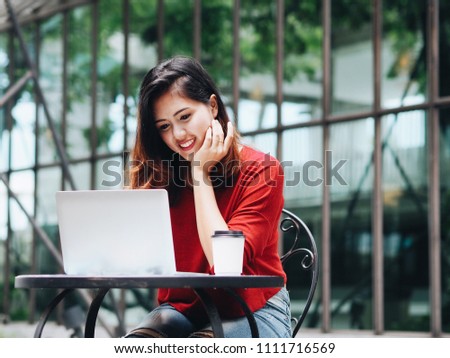 Happy Asian woman using laptop at coffee shop.
