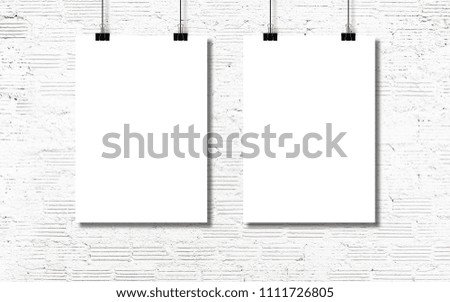 White paper or poster hanging by a clip on a white brick wall background.