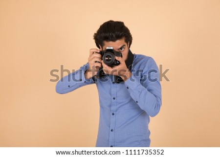 Young photographer standing holding the camera putting it on one eye taking photos on orange background.