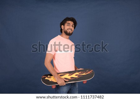 Young man holds the skateboard smiling on a blue background.