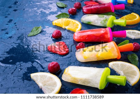 Multicolored bright fruit popsicle with strawberry, cherry, lemon, orange, lemon and mint aroma and fresh fruit on a dark blue background.
