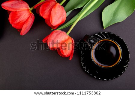 Bouquet red tulips and cup of coffee on black background. Flat lay. Mother or Woman  Day. Greeting Card. Good Morning breakfast. Copy space. Spring. 
