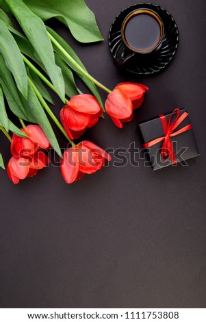 Bouquet red tulips and cup of coffee, gift, on black background. Flat lay. Mother or Woman  Day. Greeting Card. Good Morning breakfast. Copy space. Spring. 
