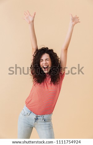 Photo of emotional excited pretty young curly woman isolated over beige background.