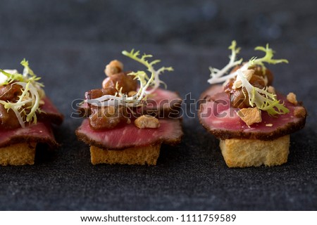 Gourmet beef filet canapes with tofu crumble, chicken bites & risee garnish on toast Royalty-Free Stock Photo #1111759589