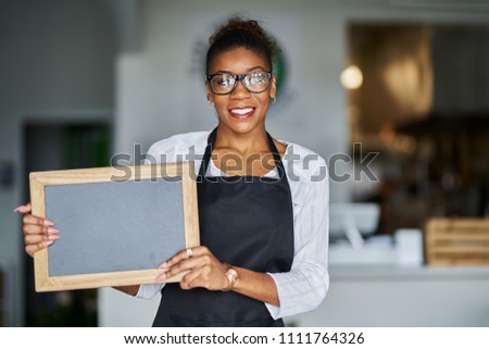 friendly african american shop assistant holding blank chalkboard slate sign