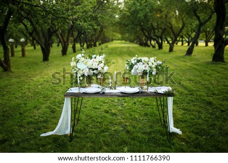 wooden table standing in an apple orchard decorated with fresh flowers Royalty-Free Stock Photo #1111766390