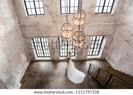 bride in a wedding dress with a long train is standing at the wall with panoramic windows Royalty-Free Stock Photo #1111797338