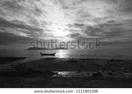 Boat float in the sea near beach in early morning and the Sun is growing up which has overlay clouds, dim light image in black and white style


