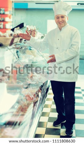 Experienced positive adult salesman offering different sausages in delicatessen shop
