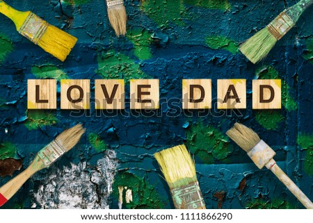 Love Dad inscription on wooden cubes with different paint brushes on a on the old painted Iron. Greetings and gifts.Holidays.