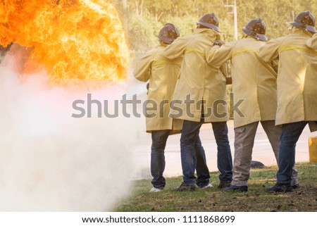 Firemen using water from hose for fire fighting at fire fight training of insurance group.Firefighter wearing a fire suit for safety under the danger training case.
