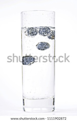 drop blueberries in a glass full of sparkling water - close up on a isolated glass