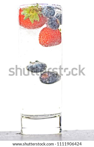 drop blueberries and strawberries in a glass full of sparkling water - close up on the isolated glass