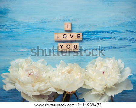 Bouquet of blooming, white peonies and the word LOVE made of wooden alphabet letters on a delicate, blue background. Top view, close-up. Concept of love and happiness. Wedding invitation