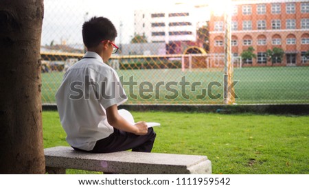 Asian school boy sitting underneath the tree and reading.
