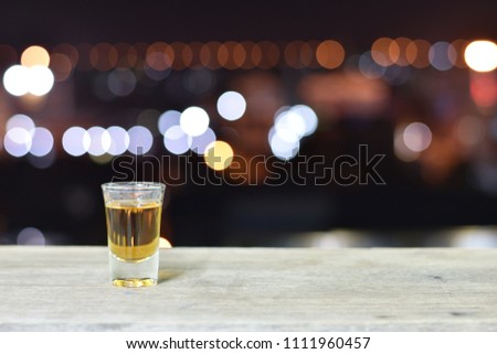 whiskey on the rocks in the Single little  glass  on old rustic wooden surface open space City night light blur bokeh background 